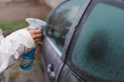 Nahaufnahme einer Frau, die ein Abtauspray auf ihr Autofenster anwendet